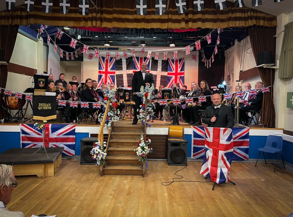 A band on the stage of the village hall surrounded by bunting and union jack flags